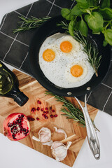 black frying pan on a black towel with three fried egg yolks in it next to a wooden cutting board with a red pomegranate on it.