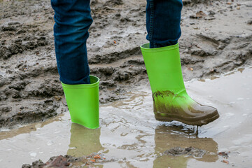 Dirty rubber boots of green color in the mud. Rubber boots of green color on a dirt road. Dirty waterproof shoes, autumn concept.