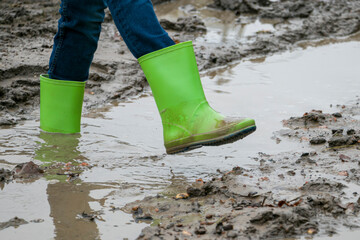 Dirty rubber boots of green color in the mud. Rubber boots of green color on a dirt road. Dirty waterproof shoes, autumn concept.