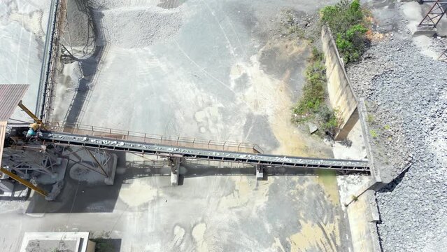 Stones and rock at mining quarry are brought over to stone crushing machine by using the conveyor belt . Aerial drone shot