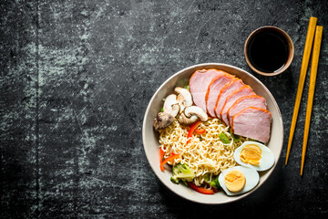 Instant noodles with vegetables, egg, ham, soy sauce and chopsticks.