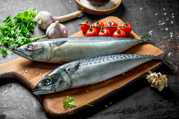Fresh raw fish mackerel on a cutting Board with tomatoes, herbs and garlic cloves.