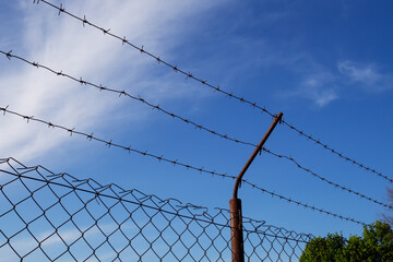 Barbed wire, triple wire, metal band with sharp spikes for fences. Rusty barbed wire against the blue sky. The concept of restricting rights and freedoms.