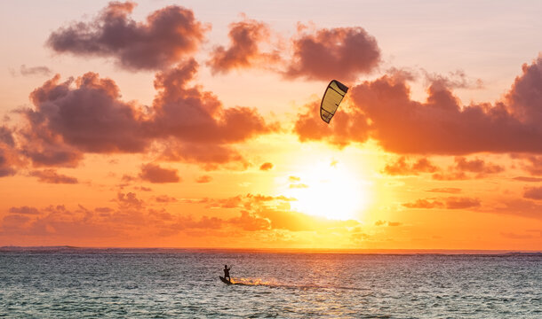 Sunset sky over the Indian Ocean bay with a kiteboarder riding kiteboard with a green bright power kite. Active sport people and beauty in Nature concept image. Le Morne beach, Mauritius.