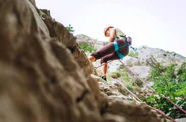 Active climber woman in protective helmet abseiling from cliff rock wall using rope with belay device and climbing harness. Active extreme sports time spending concept.