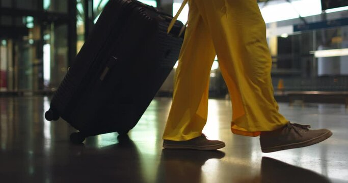 Yellow pants and gray sneakers on fast-paced female legs. Legs of a woman, she moves around the railway station. A woman hurries to her train to resort town. Travel, trip, vacation in another country.