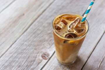 a glass of iced latte coffee with paper straw on wooden table