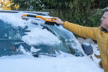 Man uses ice scrapers to thaw car windshield.