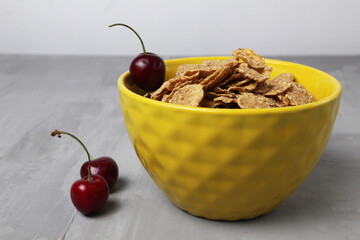 healthy breakfast oatmeal corn flakes in a bowl of yellow with cherry berries on a gray background with space for text copyspace