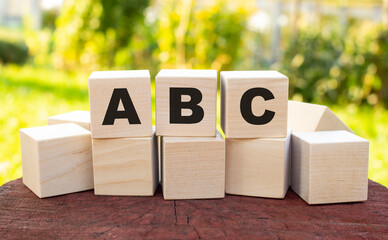 The word ABC is made up of wooden cubes lying on an old tree stump against a blurred garden background.