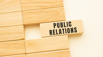PUBLIC RELATIONS text on a strip of wood lying on a white table.