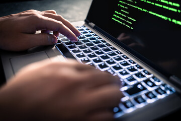 Hacker with malware software code in computer screen. Developing fraud website. Cybersecurity attack and web crime with laptop. Cyber security and data theft threat. Coder or programmer. Green text.