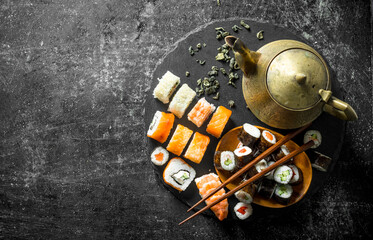 Rolls and maki on a stone stand with green tea in the teapot.