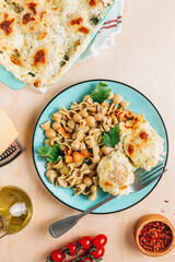 Baked cheesy meatballs casserole in the oven dish. Blue plate with with tomato and spinach pasta and meatballs