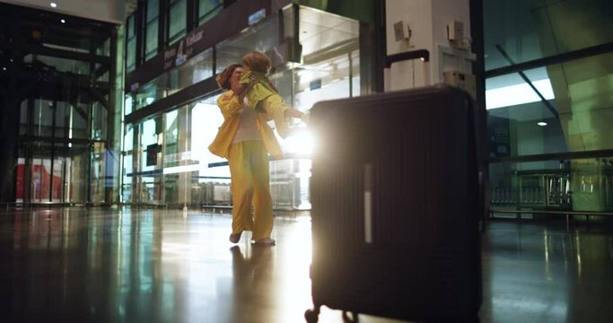 Luggage left in the foreground and a woman with a child in the background. Cinematic footage of a happy mother spinning with her son in her arms. A touching reunion of a friendly and strong family. 