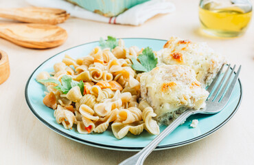 Baked cheesy meatballs casserole in the oven dish. Blue plate with with tomato and spinach pasta and meatballs