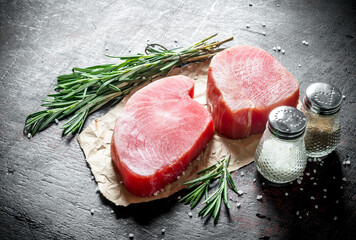 Raw tuna fillet on paper with rosemary and spices.