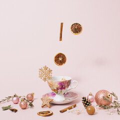 Obraz na płótnie Canvas Winter tea layout made of cup, warm tea, cinnamon stick, orange fruit, pine cone, Christmas bauble and decorative snow. Creative and healthy beverage on pastel pink background. 