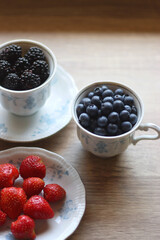 Vintage porcelain cups and plates filled with various fresh berries. Wooden background, selective focus.