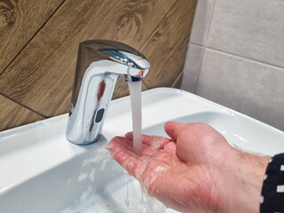 a man's hand under a stream of water from the tap in the sink. water saving concept. utilities and...