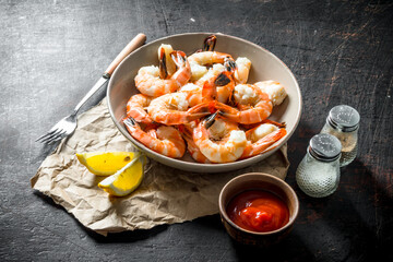 Cooked shrimps in a bowl on paper with sauce and lemon slices.