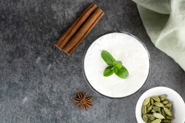 Traditional Indian yogurt drink with spices: cardamom, cinnamon stick and mint on a gray background. Top view, copy space.