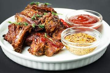 Baked ribs on a white plate. Roasted pork ribs with spices and herbs on a dark background. Food background. Side view. Copy space.