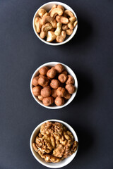 A set of nuts in white cups on a black background. Peanuts, hazelnuts and almonds. Walnut. A delicious set of nuts.