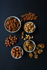 A set of nuts in white cups on a black background. Peanuts, hazelnuts and almonds. Walnut. A delicious set of nuts.