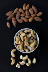 A set of nuts in white cups on a black background. Peanuts, hazelnuts and almonds. Walnut. A delicious set of nuts.