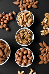 A set of nuts in white cups on a black background. Peanuts, hazelnuts and almonds. Walnut. A delicious set of nuts.