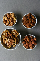A set of nuts in white cups on a black background. Peanuts, hazelnuts and almonds. Walnut. A delicious set of nuts.