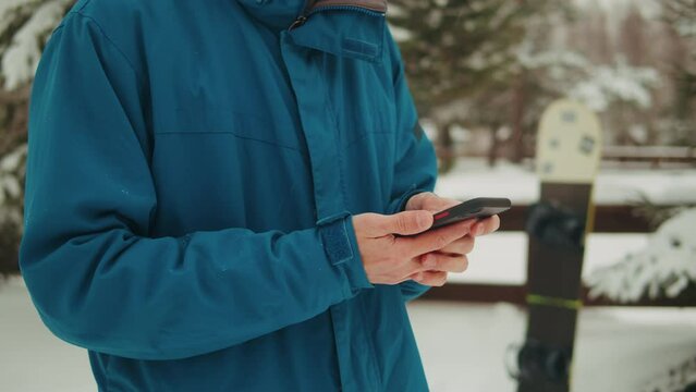 Snowboarder man rider in the snow at ski resort, using his smart phone while resting in the mountains, sport application, navigation and booking, communication, sport lifestyle