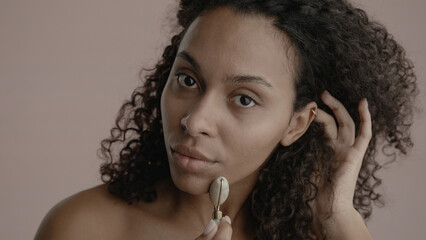 CU Headshot portrait of beautiful 20s African-American Black female cosmetic face roller against...