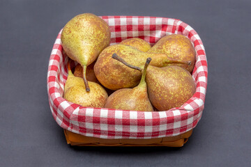 A bunch of pears are lying in a wicker wooden basket on a dark background, close-up, side view, checkered fabric.