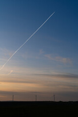 Sunset in the countryside with wind turbines on the bottom and airplane contrails in the sky