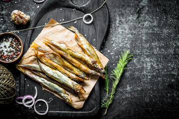 Smoked fish on a cutting Board with rosemary, twine, spices and garlic cloves.