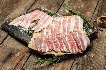 Bacon slices. Pig meat. Pork belly with rosemary on a wooden board, Keto diet food ingredients. Restaurant menu, dieting, cookbook recipe top view