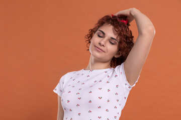 A girl corrects her curly hair with her hand. Uniform brick-colored background.