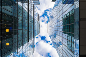 Look up to high skyscrapers corporate buildings with glass walls and reflecting beautiful cloudy sunny sky - obrazy, fototapety, plakaty