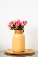 A vase of pink roses, placed on a wooden tray and isolated on a white background.