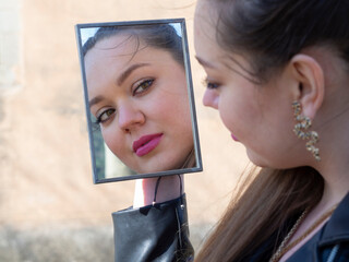 Mujer joven posando, mirándose al espejo en el exterior, con la cara blanca, mirada fija, labios...