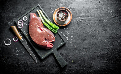 Raw liver on a cutting Board with a knife, spices and onions.