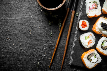 Delicious rolls with salmon and vegetables on a stone Board with soy sauce in bowl.