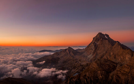 Enchanting view of the Western Alps at dawn with Monviso (3841 m) standing out against the colorful horizon and the clouds downstream that wrap it like a blanket. Monviso Park. August