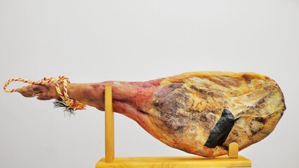 A front leg of Serrano ham mapped on a wooden stand on a white background.