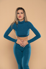 Naklejka premium Close up woman holding belly, feeling discomfort, health problem concept, unhappy girl standing at beige background, suffering from stomachache, gastritis, abdominal pain, menstrual period