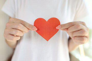 Female in white t-shirt holds red heart in her hands in front of her body.