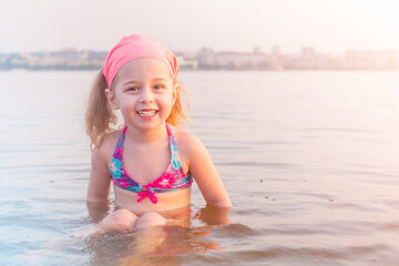 A little girl is bathing in the river in the city. A child in a swimsuit in the water in the summer.