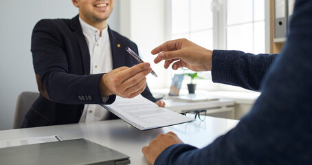 Two young people make a business deal and sign a contract agreement. Smiling agent sitting at his...